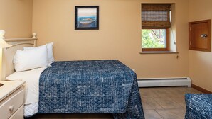 Une chambre à coucher avec un lit, une table de chevet, une fenêtre avec des stores, un tableau au mur et une porte.