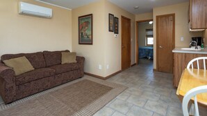 A living room with a patterned sofa, a kitchen area with wooden cabinets, and a dining table. - A Suite Place .5 mi from Beach (Michigan City)