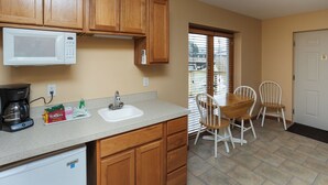 A kitchen with wooden cabinets, a microwave, a coffee maker, and a dining area with chairs and a table. - A Suite Place .5 mi from Beach (Michigan City)