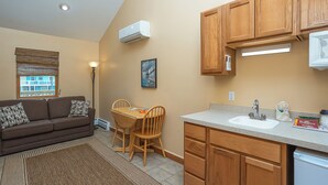 A compact living space with a kitchenette, a dining area with a table and chairs, a sofa with patterned cushions, and a view through a window.