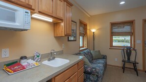 A compact kitchen with wooden cabinets, a microwave, a sink, and a window with blinds. - A Suite Place .5 mi from Beach (Michigan City)
