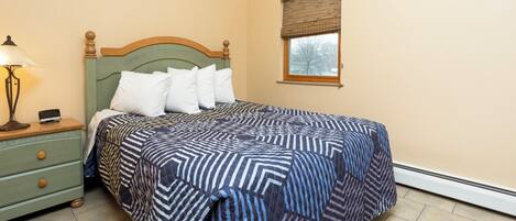 A bedroom with a bed, a nightstand, a lamp, and a window with blinds.