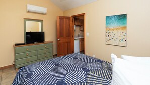 A bedroom with a bed, a dresser, a television, a painting, and a ceiling fan.