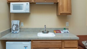 A compact kitchenette with wooden cabinets, a microwave, a coffee maker, a sink, and a refrigerator. - A Suite Place .5 mi from Beach (Michigan City)