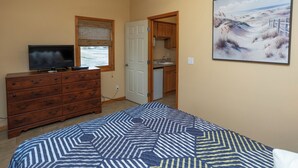 Een slaapkamer met een bed, een dressoir, een televisie en een schilderij van een strand.