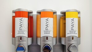 Vier cilindrische verpakkingen van Paya haarverzorgingsproducten in verschillende kleuren.