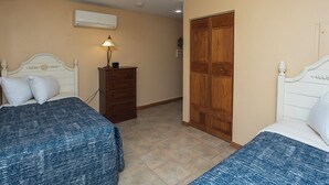 Une chambre avec deux lits, une commode, un ventilateur de plafond et une armoire en bois.