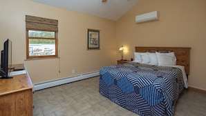 Un dormitorio con cama, ventilador de techo, ventana con persianas, un cuadro enmarcado y un equipo de aire acondicionado.