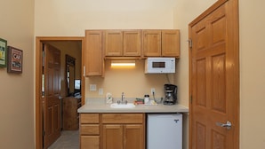 Cocina compacta con armarios de madera, microondas integrado, cafetera y refrigerador pequeño.