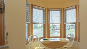 Un rincón comedor con una mesa y dos sillas, ventanas amplias con persianas y una lámpara de techo.