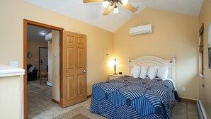 A bedroom with a bed, a ceiling fan, an air conditioning unit, and a door leading to another room. - A Suite Place .5 mi from Beach (Michigan City)