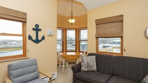 A cozy living room with a gray sofa, a wooden chair, a dining table, and a large anchor decoration on the wall. - A Suite Place .5 mi from Beach (Michigan City)