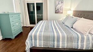 A bedroom with a bed, a dresser, a ceiling fan, and a door leading to a balcony. - Carolina Beach Ocean View Retreat w/ Beach Access! (Carolina Beach)