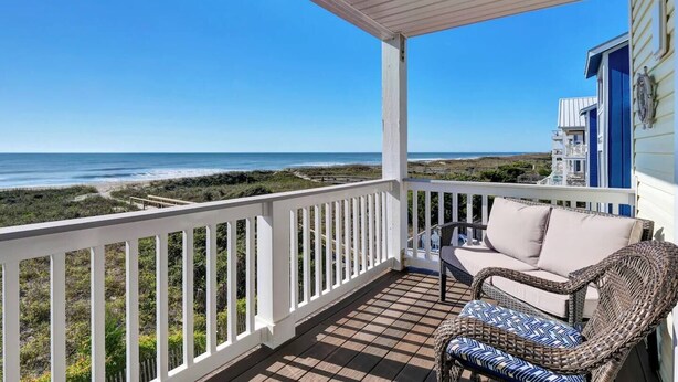 A covered porch with a view of the ocean, a wicker chair, and a building with blue siding. - Carolina Beach Ocean View Retreat w/ Beach Access! (Carolina Beach)