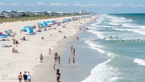 A beach with people sunbathing, swimming, and walking along the shore. - Carolina Beach Ocean View Retreat w/ Beach Access! (Carolina Beach)