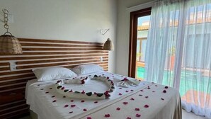 Un dormitorio con cama, cabecero de madera y ventana con cortinas translúcidas.