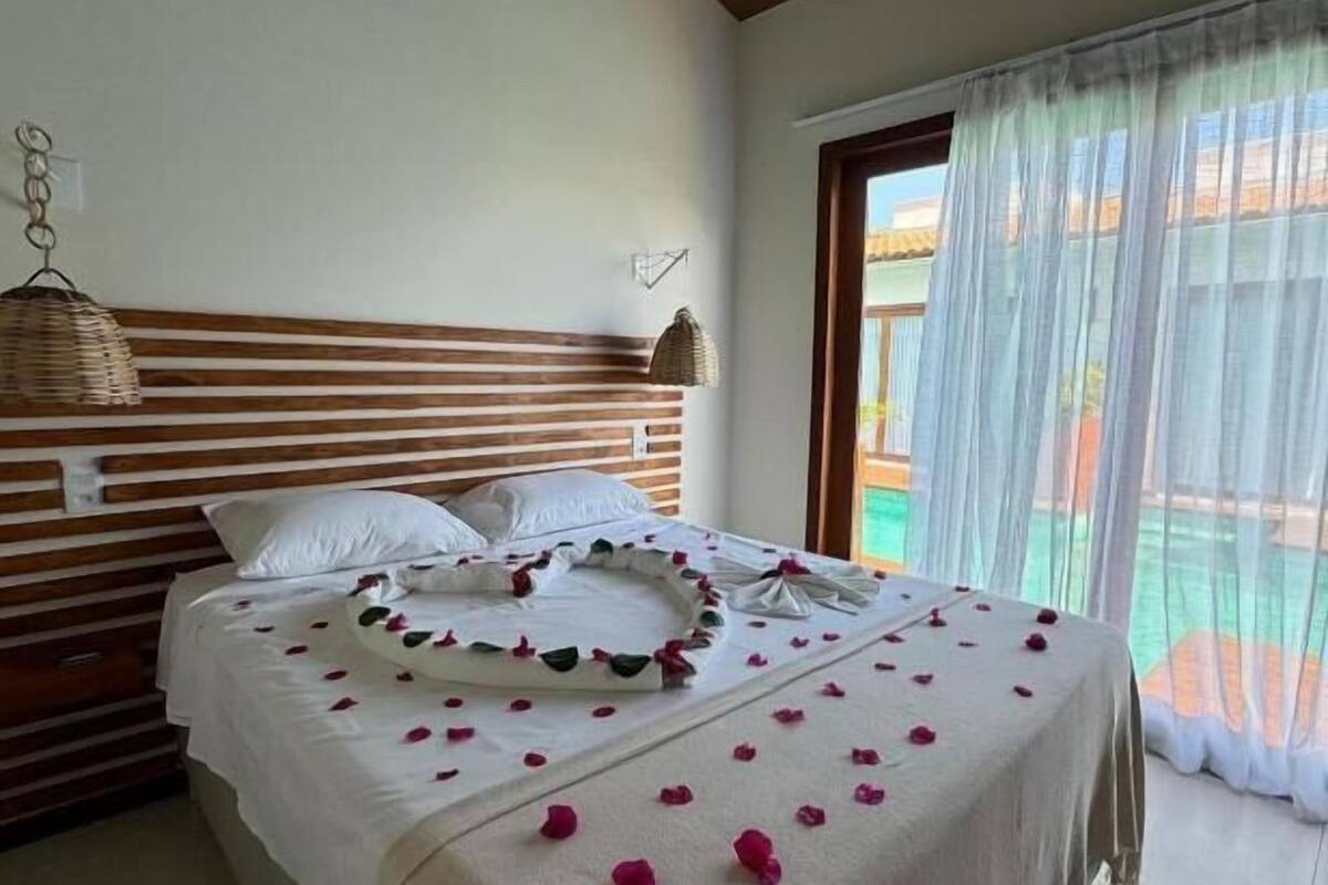 Un dormitorio con cama, cabecero de madera y ventana con cortinas translúcidas.