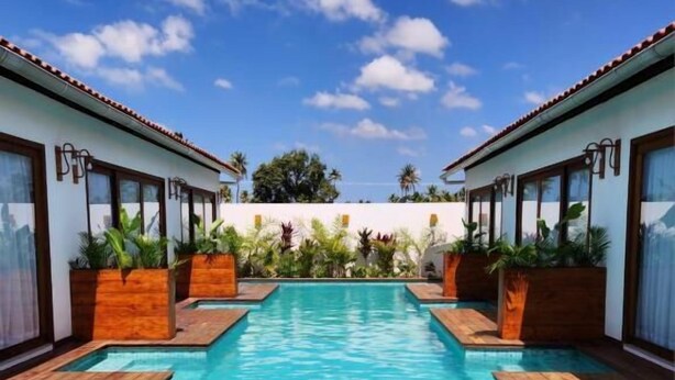 Una piscina con bordes de madera, rodeada por edificios de dos pisos con ventanas amplias y plantas en macetas.