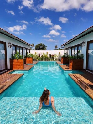 Una piscina con bordes de madera, rodeada por edificios de dos pisos con ventanas amplias y plantas en macetas.