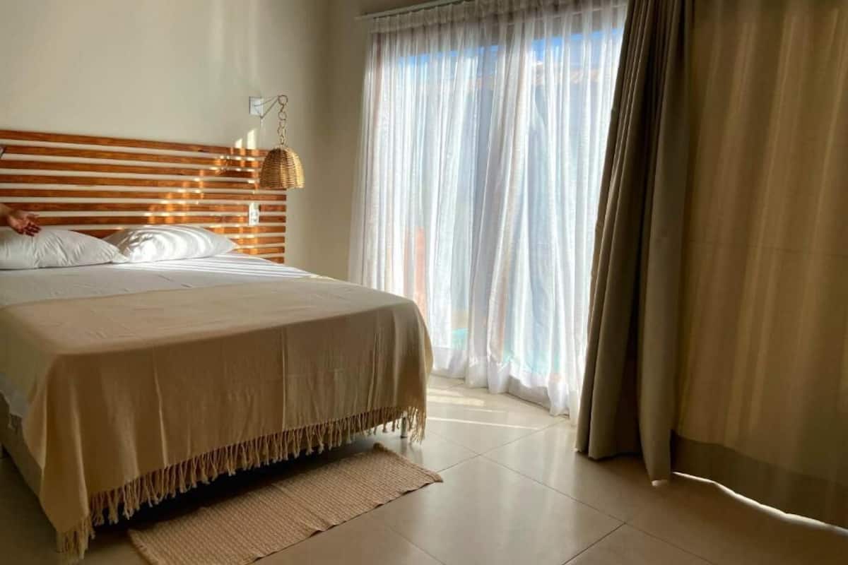 Un dormitorio con cama, una cesta colgante y cortinas de gasa.