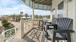 A covered porch with wooden flooring, white railings, and two Adirondack chairs. - Calypso Breeze | Gulf Views (Orange Beach)