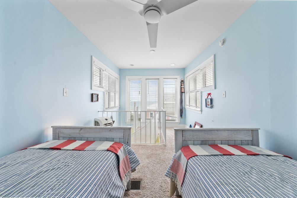 Une chambre avec deux lits, un ventilateur de plafond et une fenêtre avec des stores.