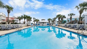 A swimming pool with lounge chairs and palm trees, surrounded by buildings. - Calypso Breeze | Gulf Views (Orange Beach)