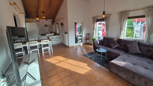 Ein geräumiger Wohnbereich mit einer Couch, einem Esstisch und Stühlen. Ein Fernseher ist an der Wand montiert, und es gibt ein Fenster mit Vorhängen.