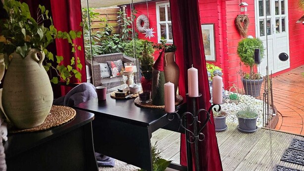 Ein gemütliches Zimmer mit einem großen Fenster, einem Tisch mit Kerzen und Blick auf ein rotes Haus.