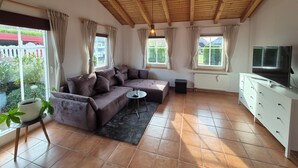 Ein Wohnzimmer mit Holzboden, einer Couch, einem kleinen Tisch, einem Fernseher und einem Fenster mit Vorhängen.