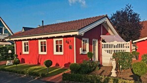 Ein rotes Haus mit weißem Zaun, ein kleiner Garten und ein klarer Himmel.