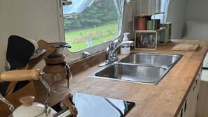 Eine kleine Küche mit Wasserkocher, Spüle und Fenster mit Blick auf eine grüne Landschaft.