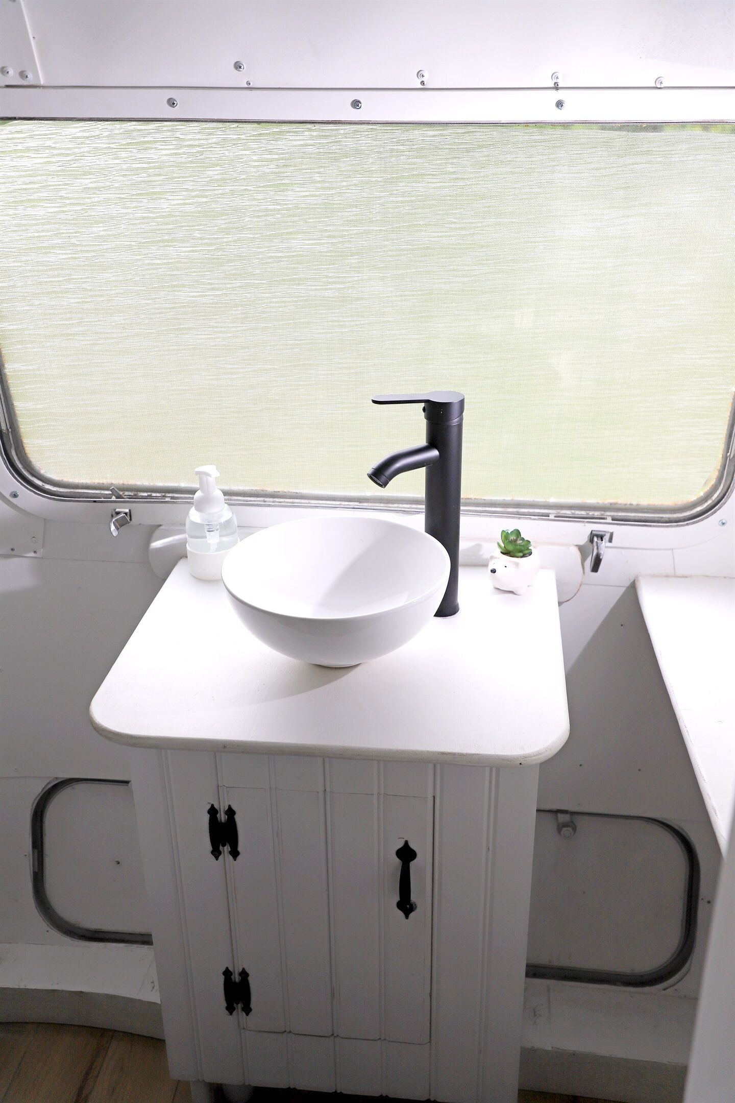 Une salle de bain blanche avec un lavabo blanc, un robinet noir et une petite plante en pot.