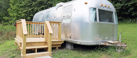 Experience the freedom of a vintage Airstream trailer, elevated on a wooden deck amidst lush greenery.