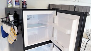 Ein kompakter Kühlschrank mit zwei Türen, einem Fach mit Reinigungsmitteln und einem aufgehängten Handtuch.