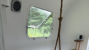Eine Holzbank mit einer Taue und einer kleinen Fensteröffnung mit Blick auf Grünflächen, sowie ein weißer Heizkörper.