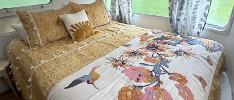 Una cama con colcha estampada y dos almohadas, una ventana con cortinas y suelo de madera.