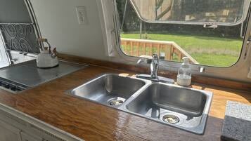 Eine Küche mit doppelter Spüle, Wasserkocher und Fenster mit Blick auf eine Holzterrasse.
