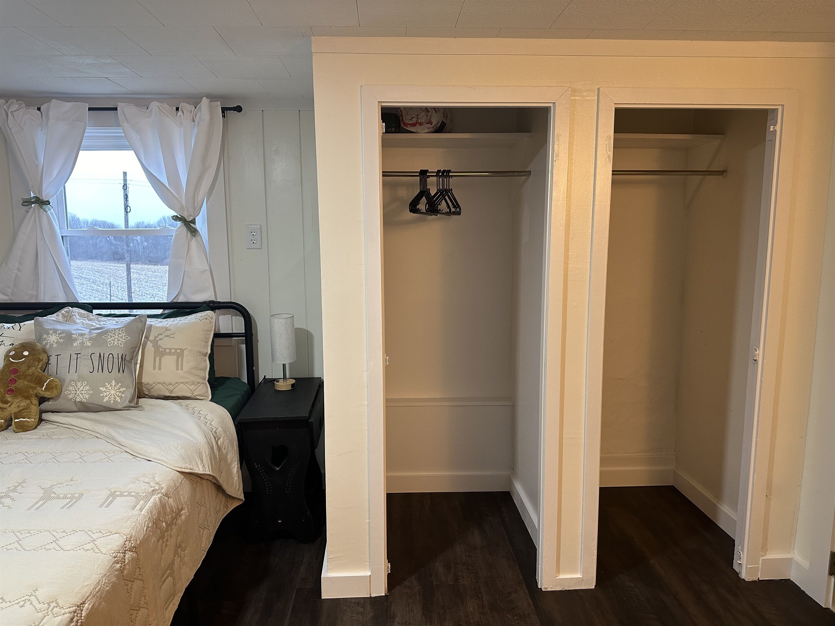 Un dormitorio con cama, mesita de noche, lámpara y armario con ropa colgada.