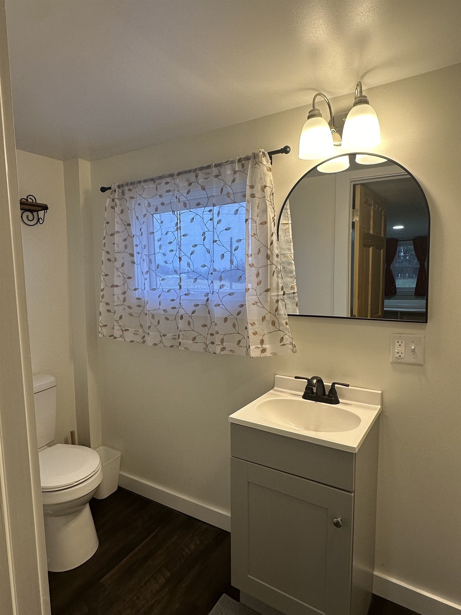 Ein Badezimmer mit Toilette, Waschbecken und einem Fenster mit einem blattgemusterten Vorhang.