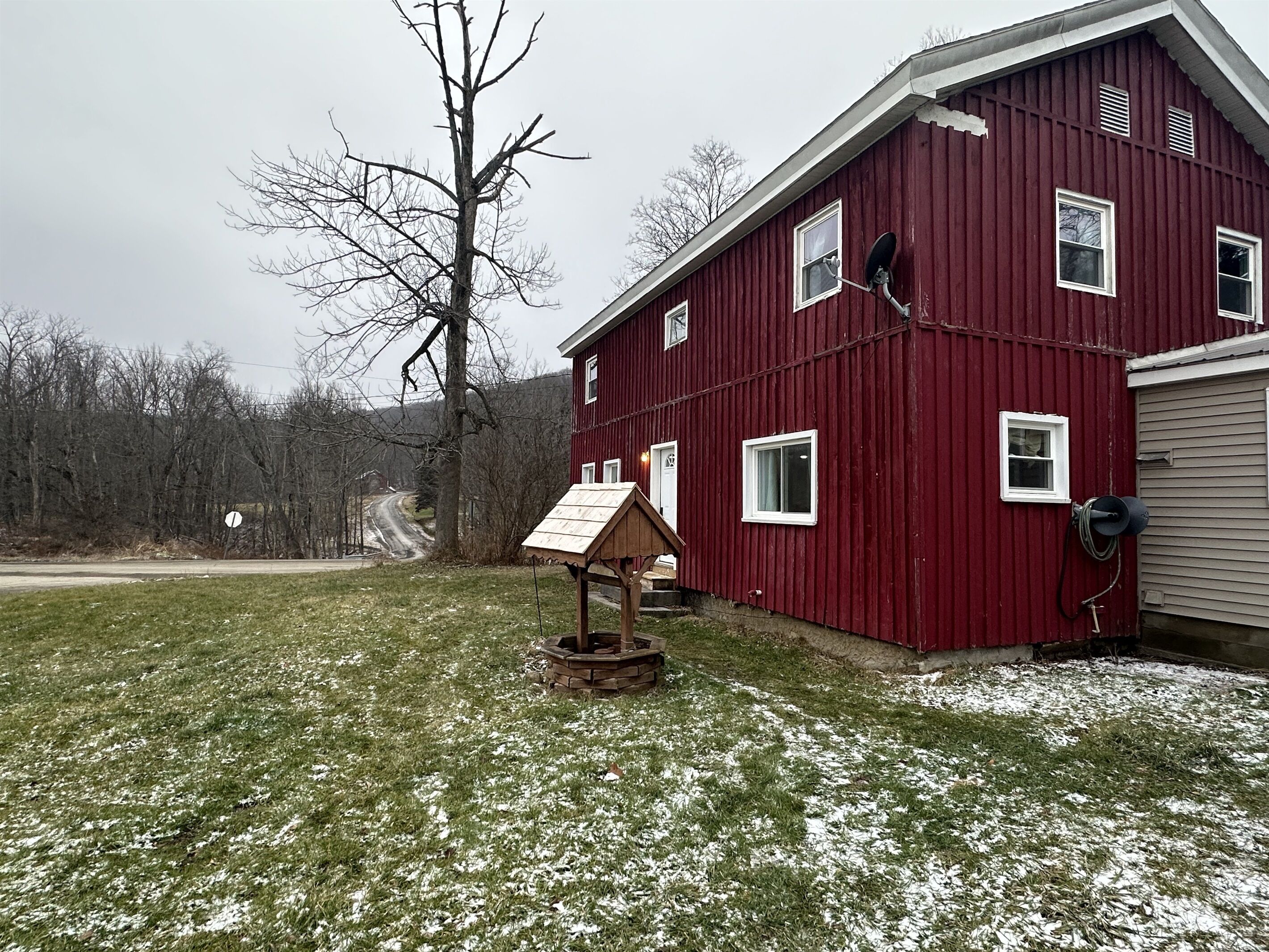 Une grange rouge avec des dépendances en bois, un chemin de gravier et une pelouse recouverte de neige.