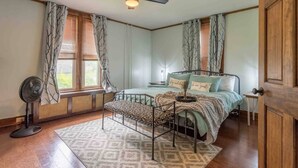 Ein Schlafzimmer mit einem Bett, einem Nachttisch, einem Ventilator und einem Fenster mit Vorhängen.