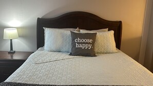 A neatly made bed with a quilted cover and two pillows, one with the text "choose happy." A bedside lamp is on to the left. - *NEW*Hops House-Sleeps10-8Mi.toCDP&15Mi.toASV (Hartwick)