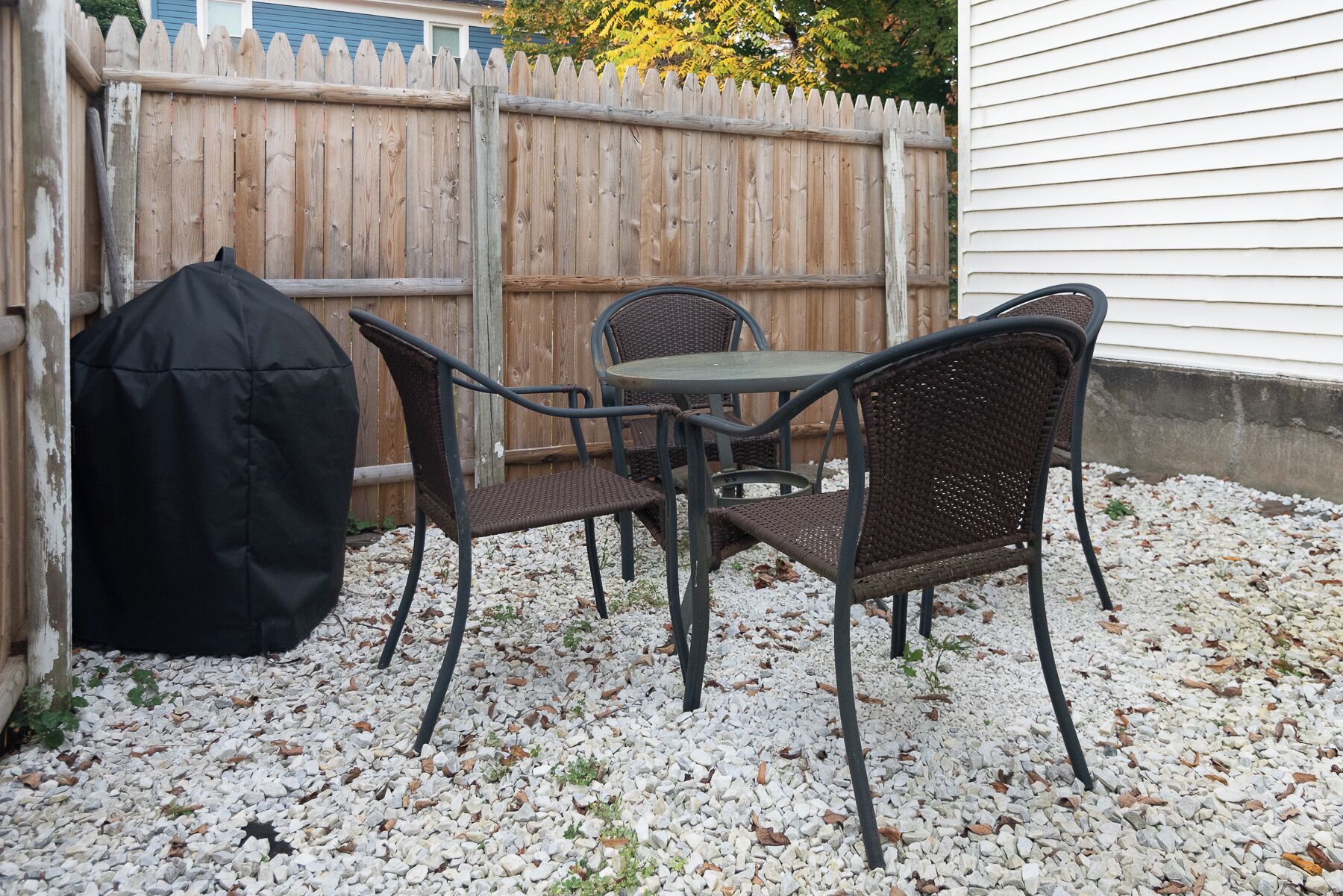 A patio with a table and chairs, a grill, and a wooden fence.