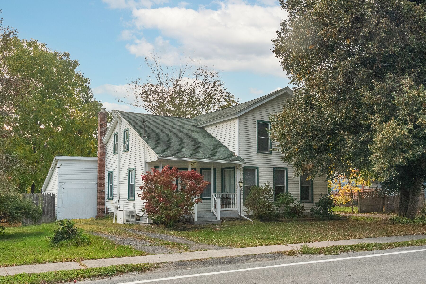 A two-story house with a front porch, a garage, and a large tree to the right.