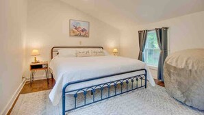Un dormitorio con cama, lámparas de noche, una ventana con cortinas y un cuadro en la pared.