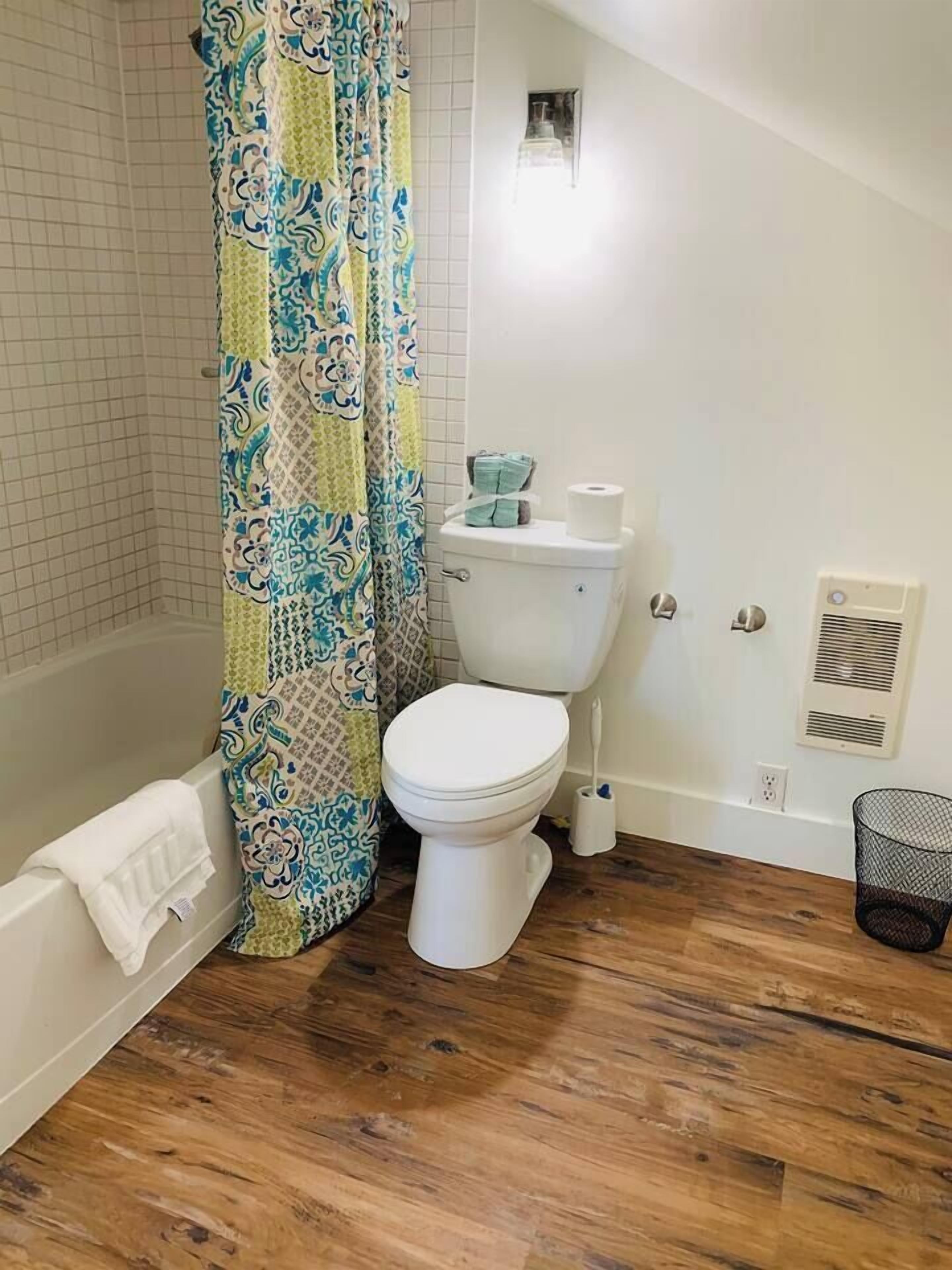 Un bagno con il water bianco, una tenda da doccia fantasia, una vasca e un pavimento in legno.