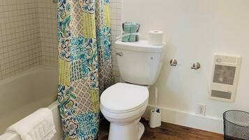 Un bagno con il water bianco, una tenda da doccia fantasia, una vasca e un pavimento in legno.