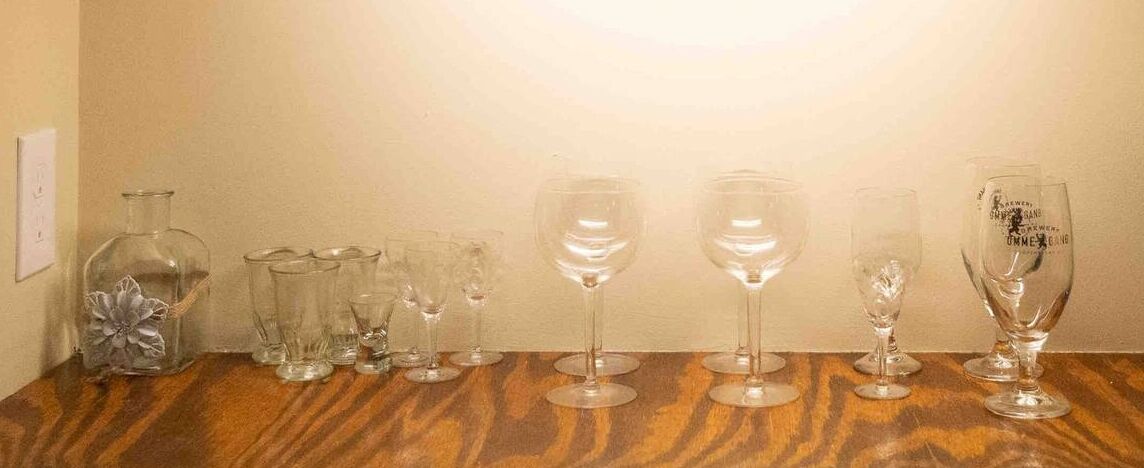 A wooden table with various glassware, including wine glasses and a decorative bottle, against a plain wall.