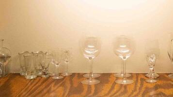 A wooden table with various glassware, including wine glasses and a decorative bottle, against a plain wall.